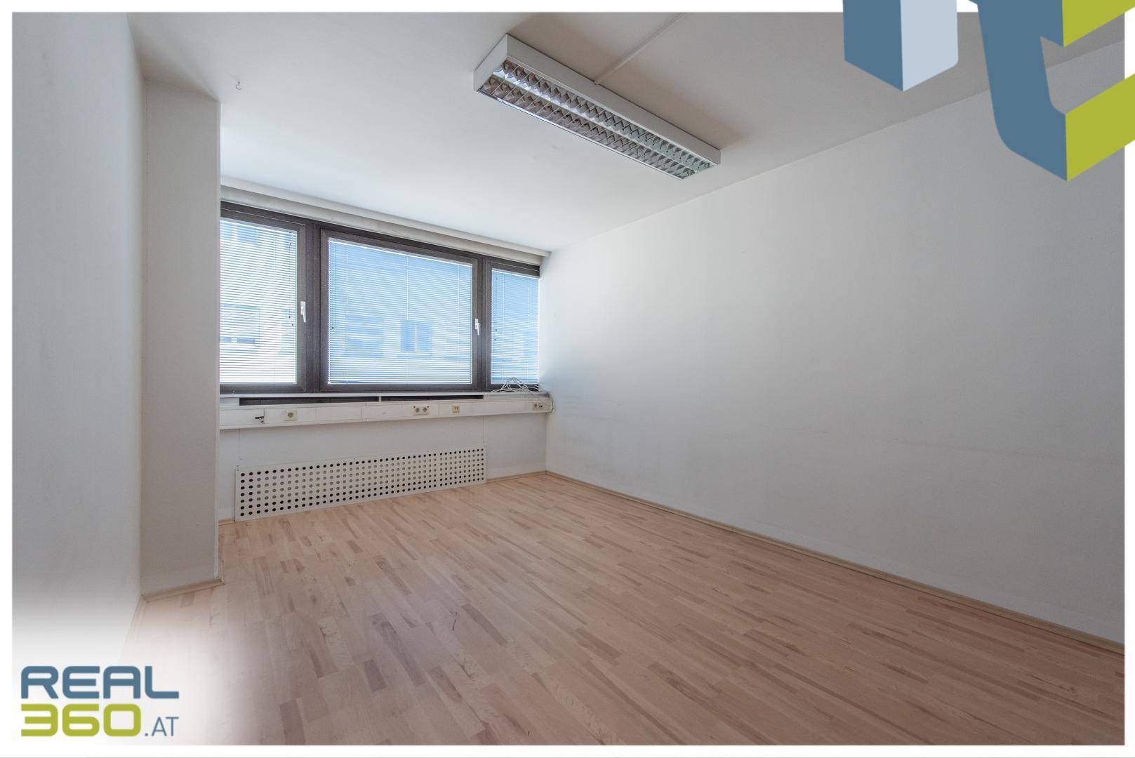 Helles Büro mit Holzboden, großen Fenstern und Blick auf die umliegenden Gebäude.