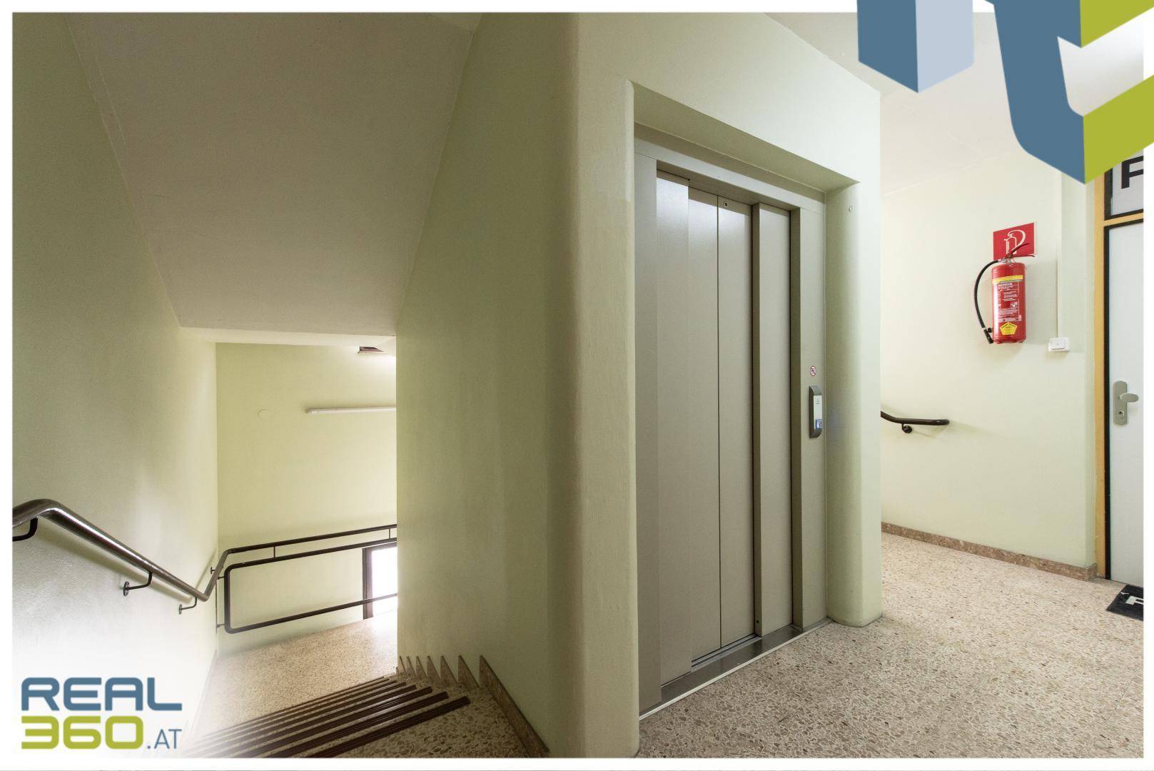Treppenhaus mit Aufzug, Handläufen und Terrazzoboden in einem Mehrfamilienhaus.