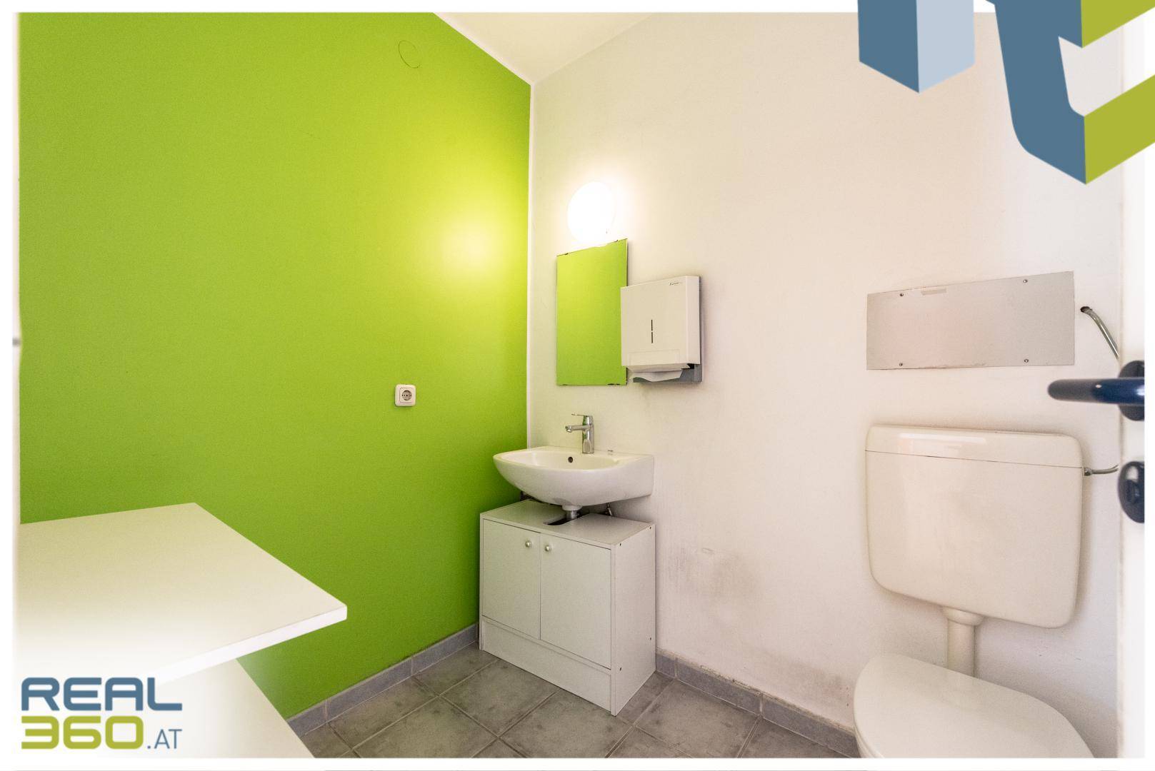 Modernes WC mit grüner Akzentwand, Waschbecken und wandhängender Toilette.