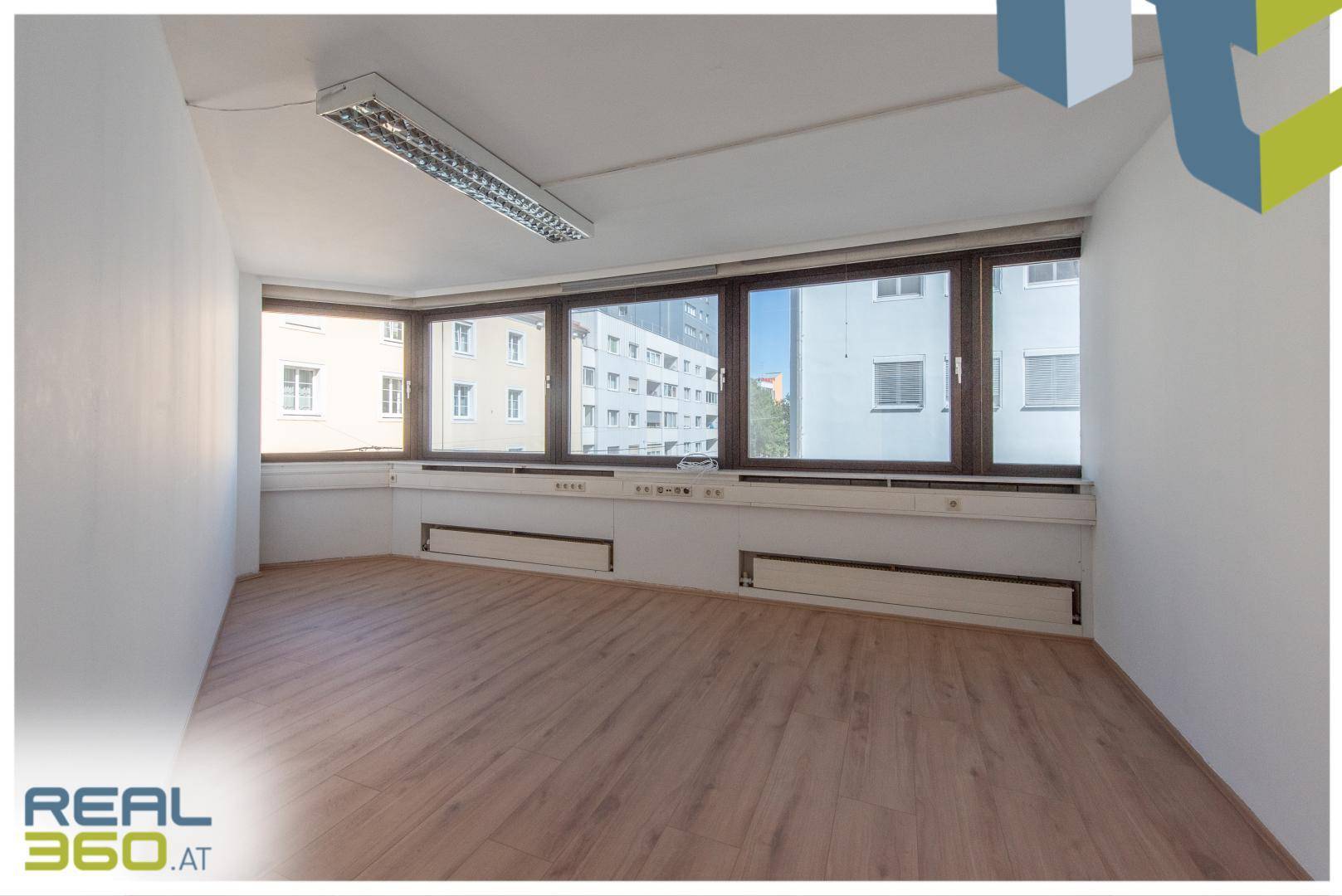 Geräumiges Eckbüro mit Holzboden, großen Fenstern und weitem Blick auf die Stadt.