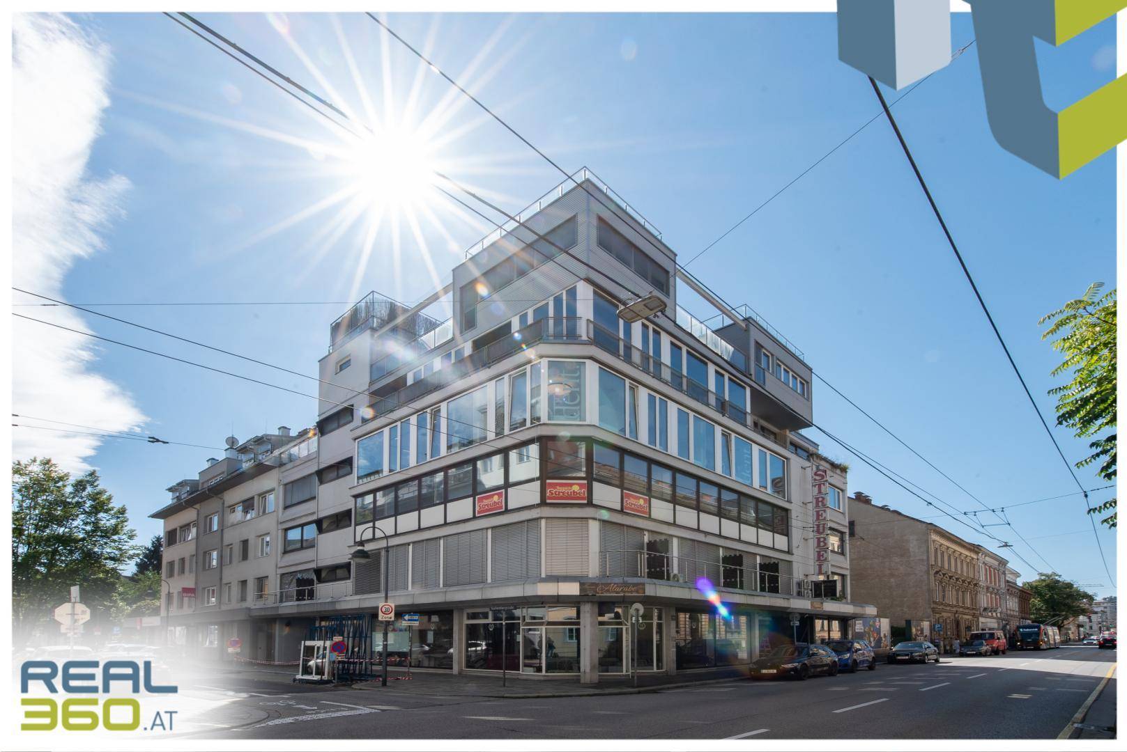 Modernes Eckgebäude mit großen Glasflächen und Geschäften im Erdgeschoss.