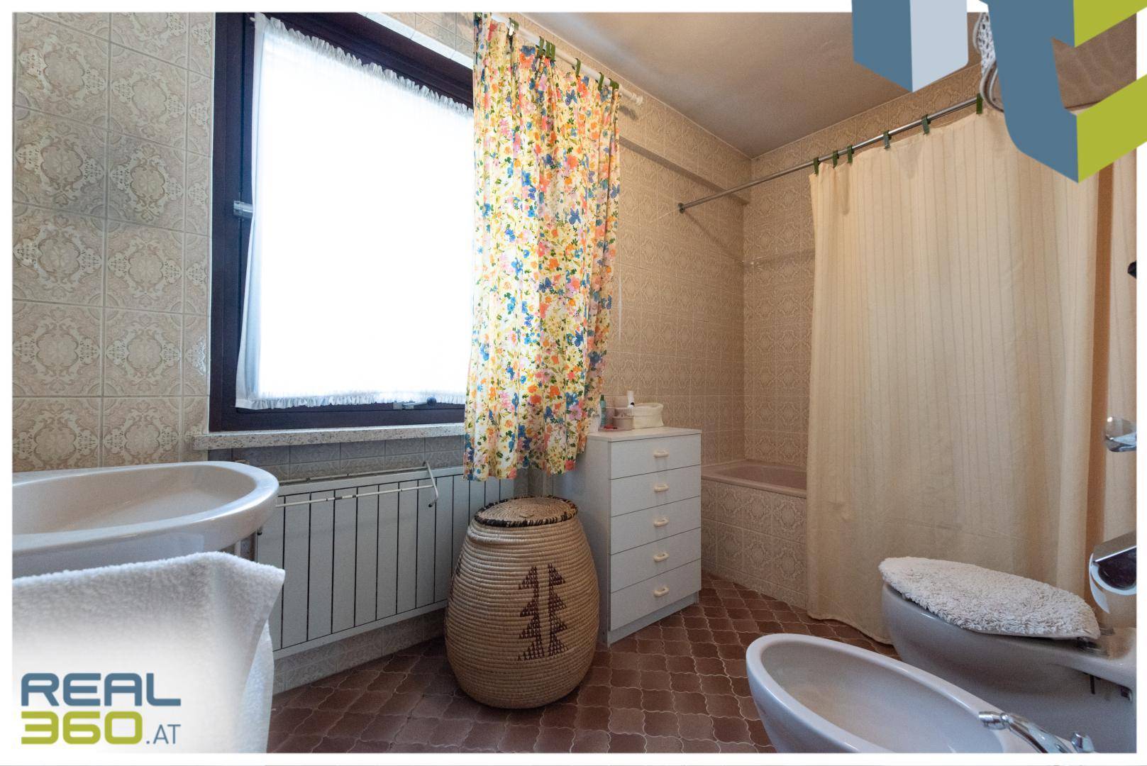 Badezimmer im Stil der 80er Jahre mit Badewanne, Bidet und Fenster für Tageslicht.