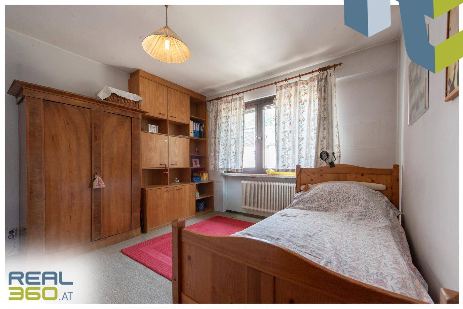 Gemütliches Schlafzimmer mit Einzelbett, Holzmöbeln und Fensterblick ins Grüne.