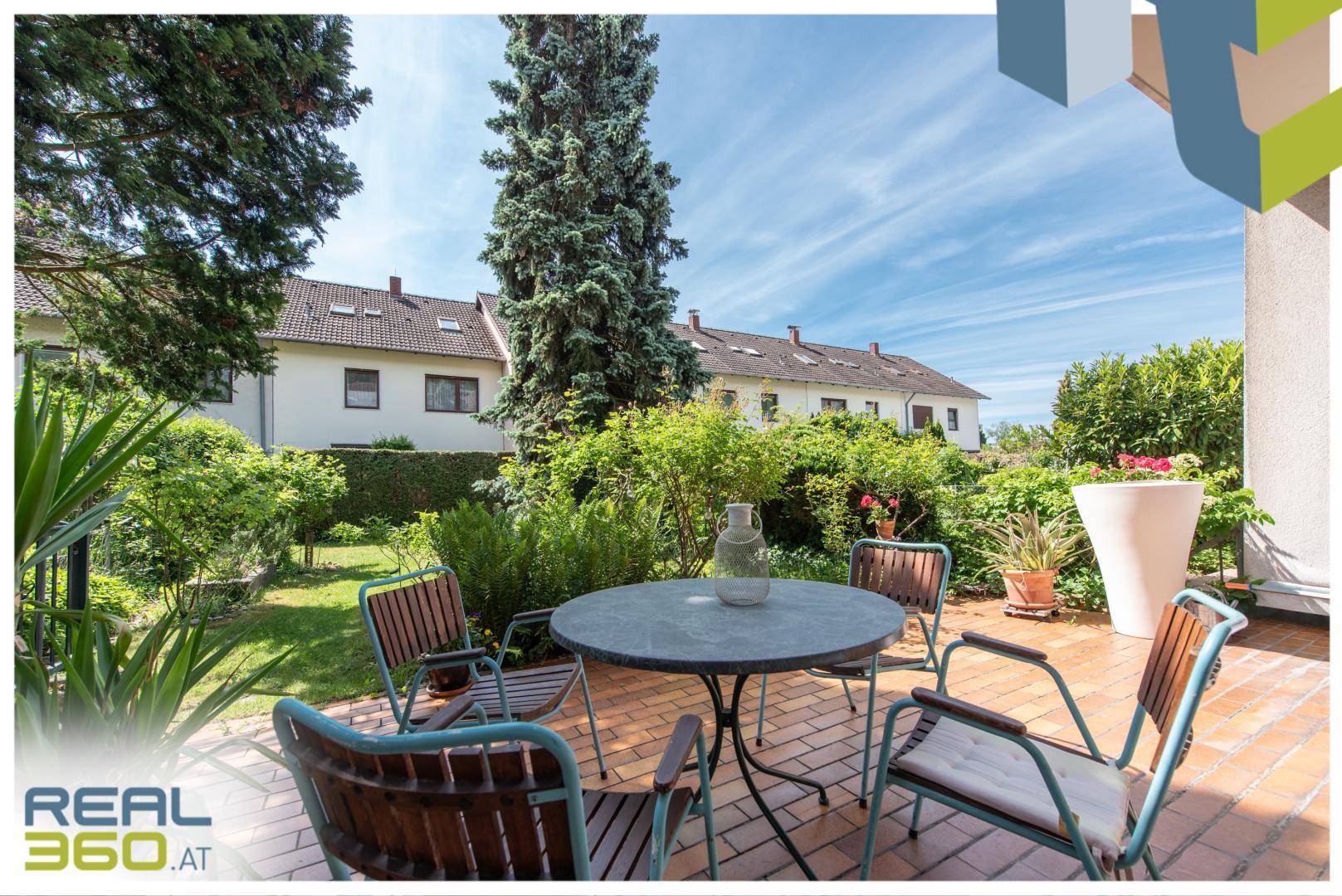 Sonniger Terrassenbereich mit Gartenmöbeln und Blick auf den gepflegten Garten unter blauem Himmel.