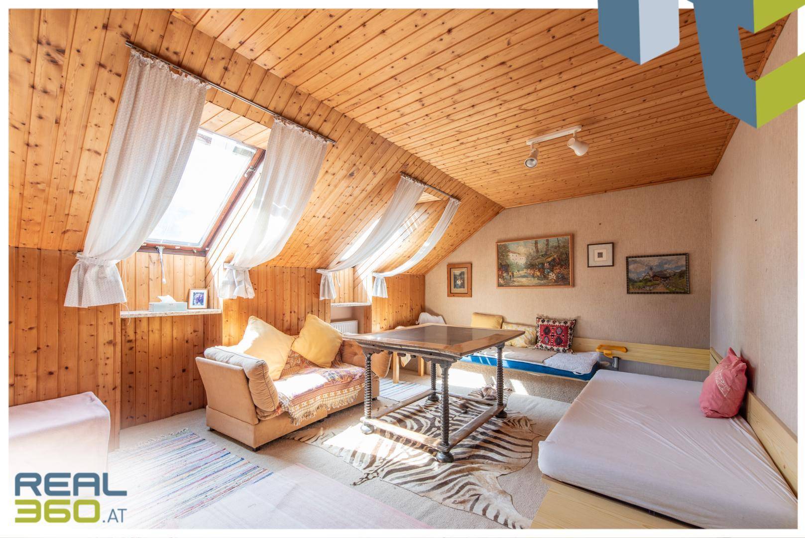 Helles Dachzimmer mit Holzverkleidung, mehreren Dachfenstern und einer gemütlichen Sitzecke.