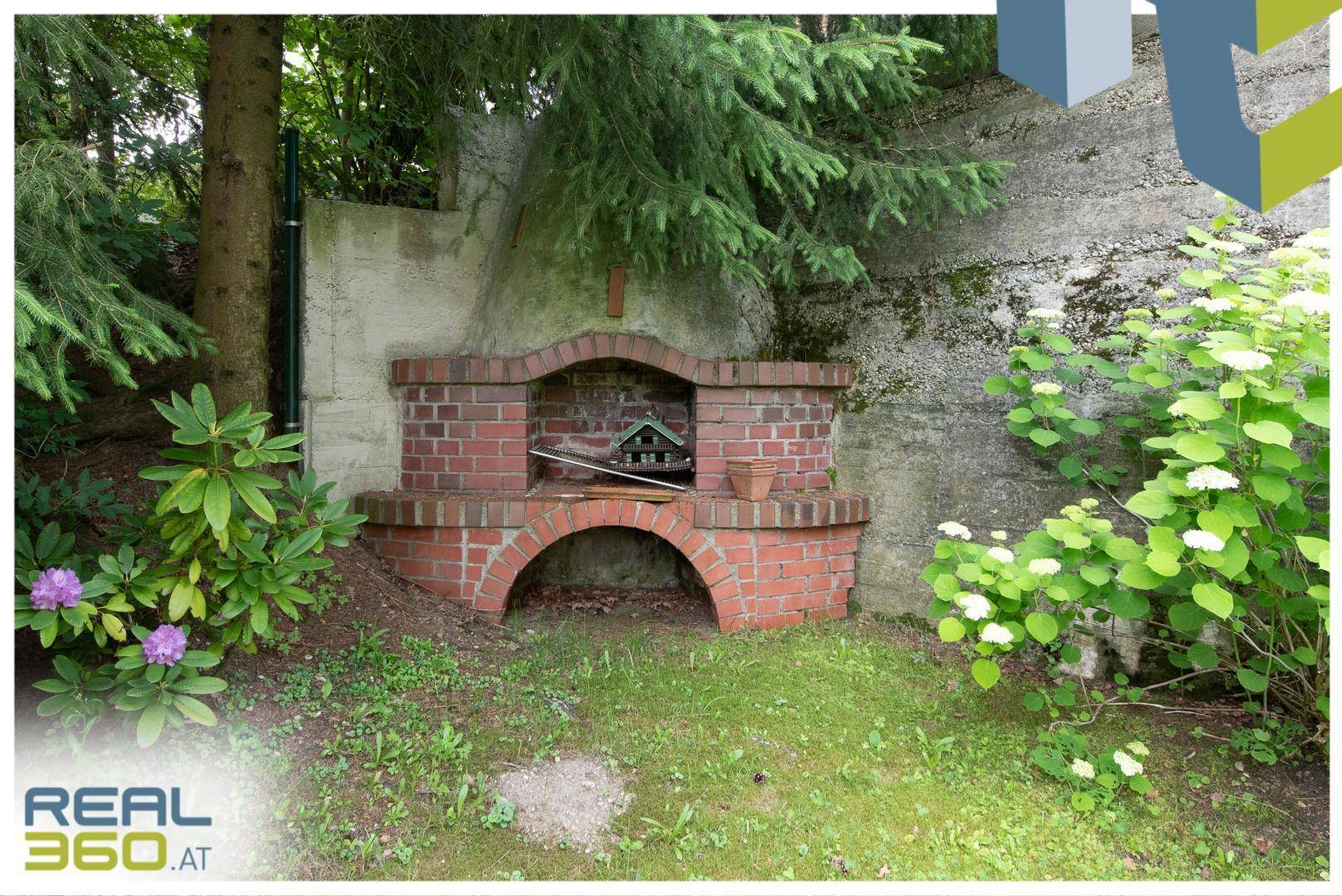 Gemütlicher Grillplatz aus Ziegelsteinen im Garten, umgeben von Sträuchern und Bäumen.