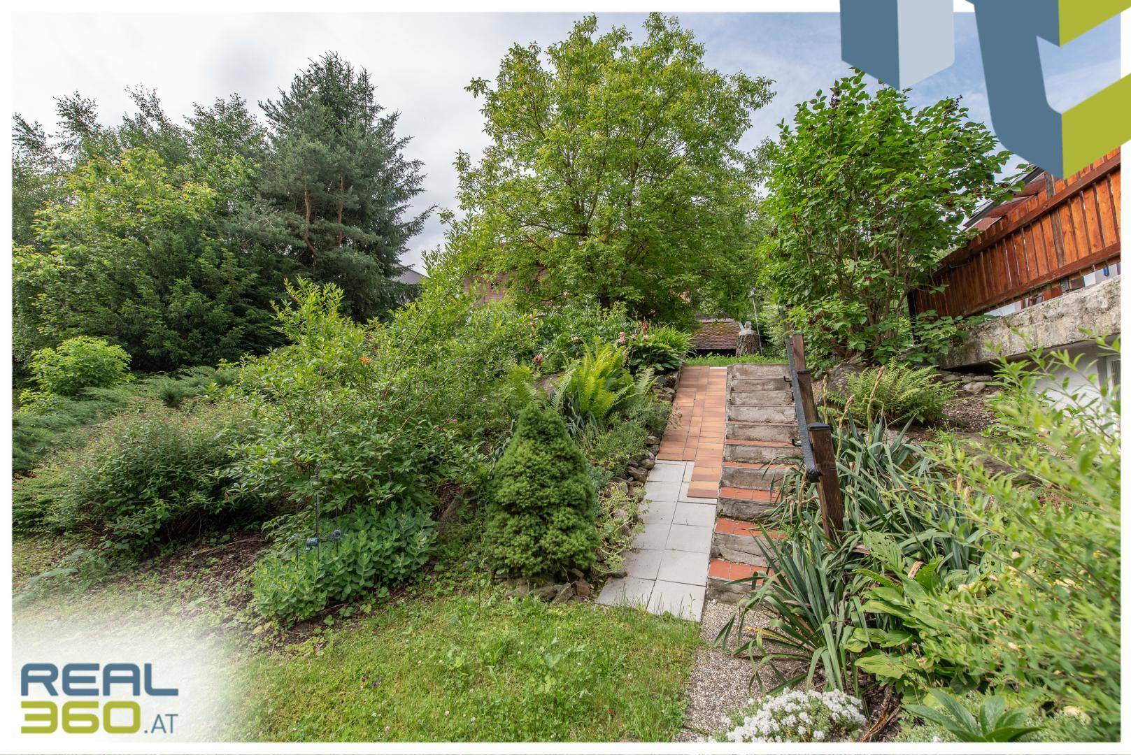 Terrassierter Gartenbereich mit Treppenweg, umgeben von vielfältiger Bepflanzung und Sträuchern.