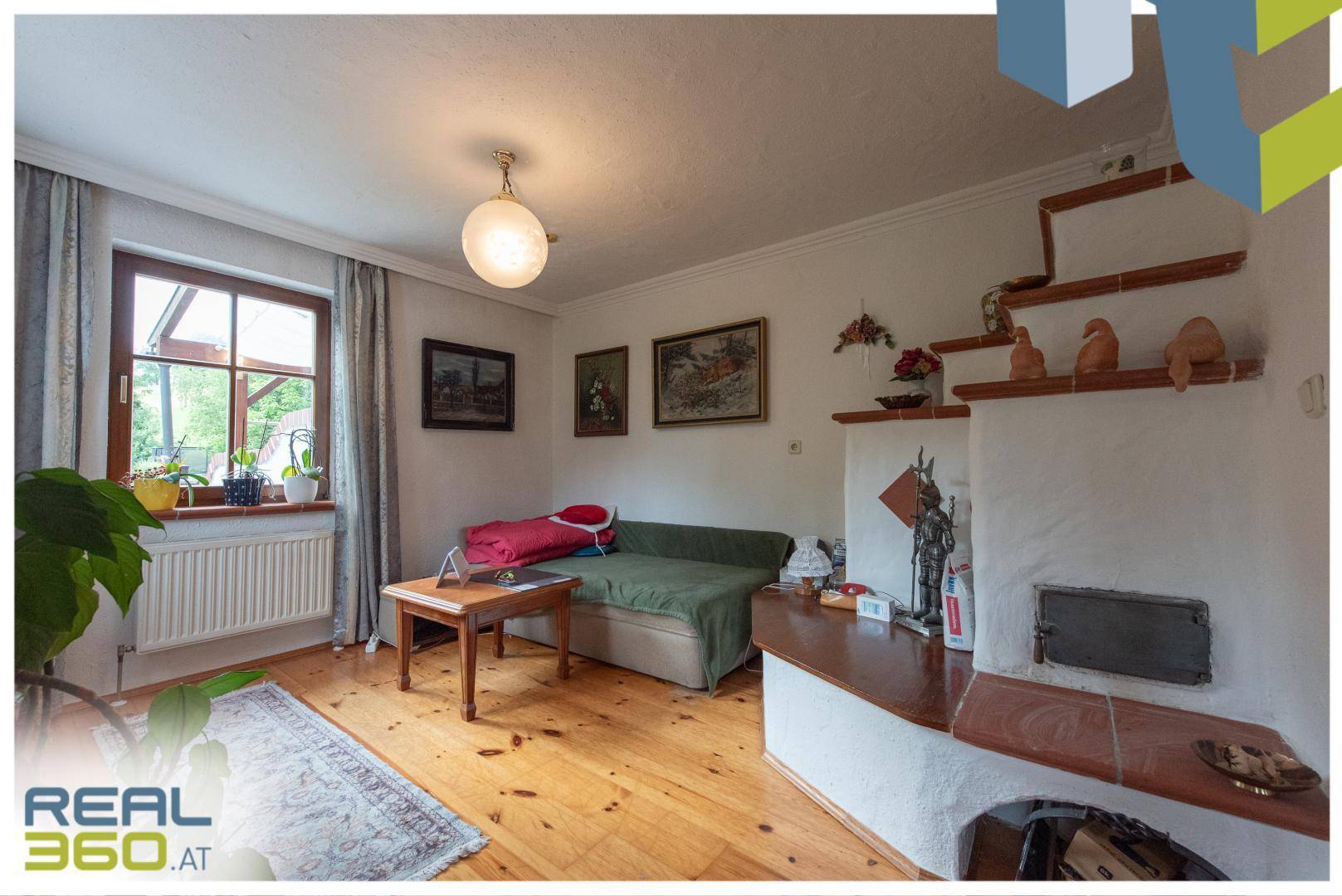 Gemütliches Wohnzimmer mit Holzboden, Kachelofen und Blick auf die grüne Umgebung.