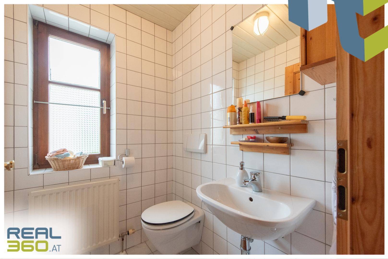 Kleines Badezimmer mit WC, Waschbecken, Fenster und weißen Wandfliesen.