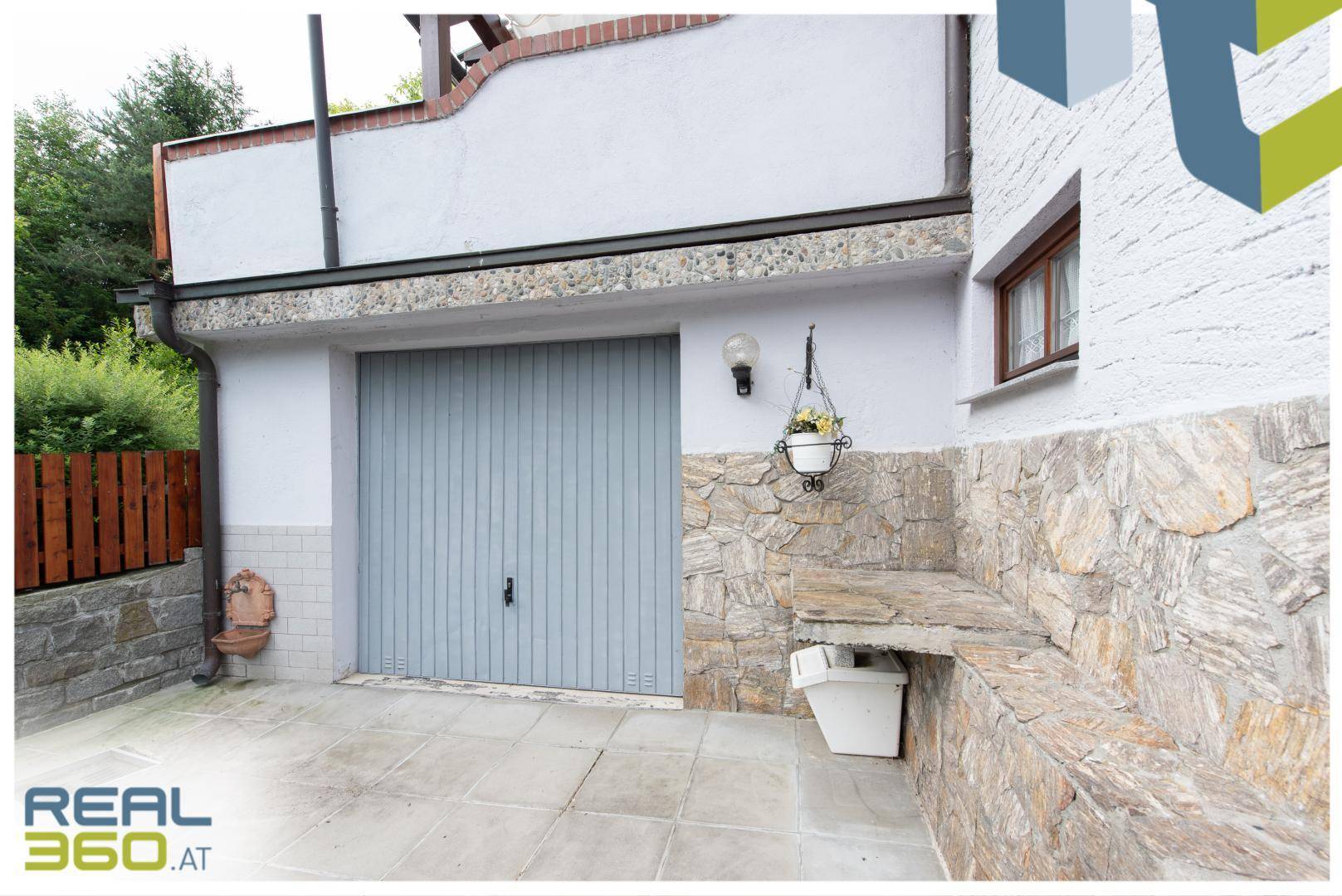 Garageneinfahrt mit hellblauer Tür und einer Fassadenverkleidung aus Naturstein.