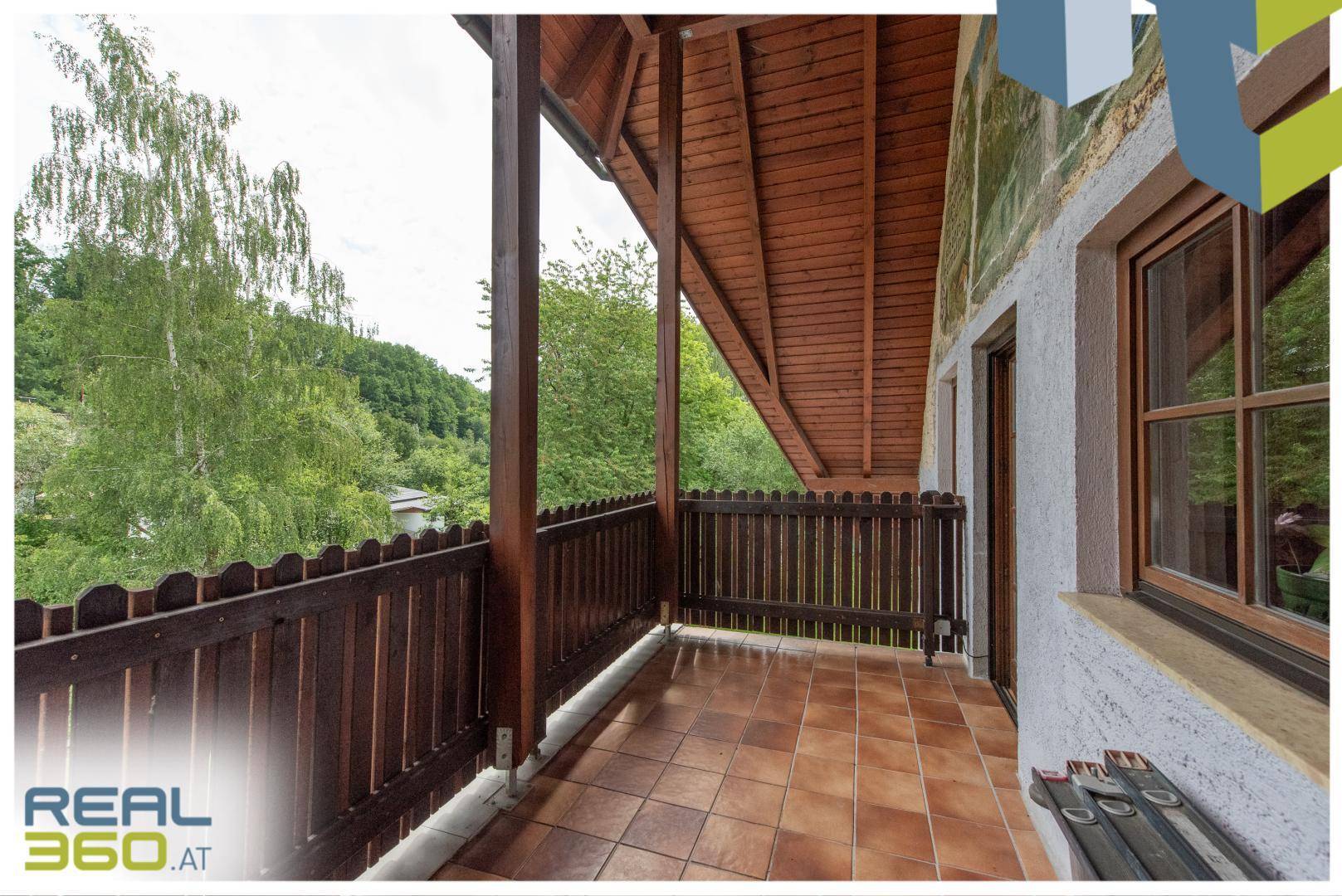 Balkon mit Holzgeländer und Fliesenboden, bietet einen grünen Ausblick.