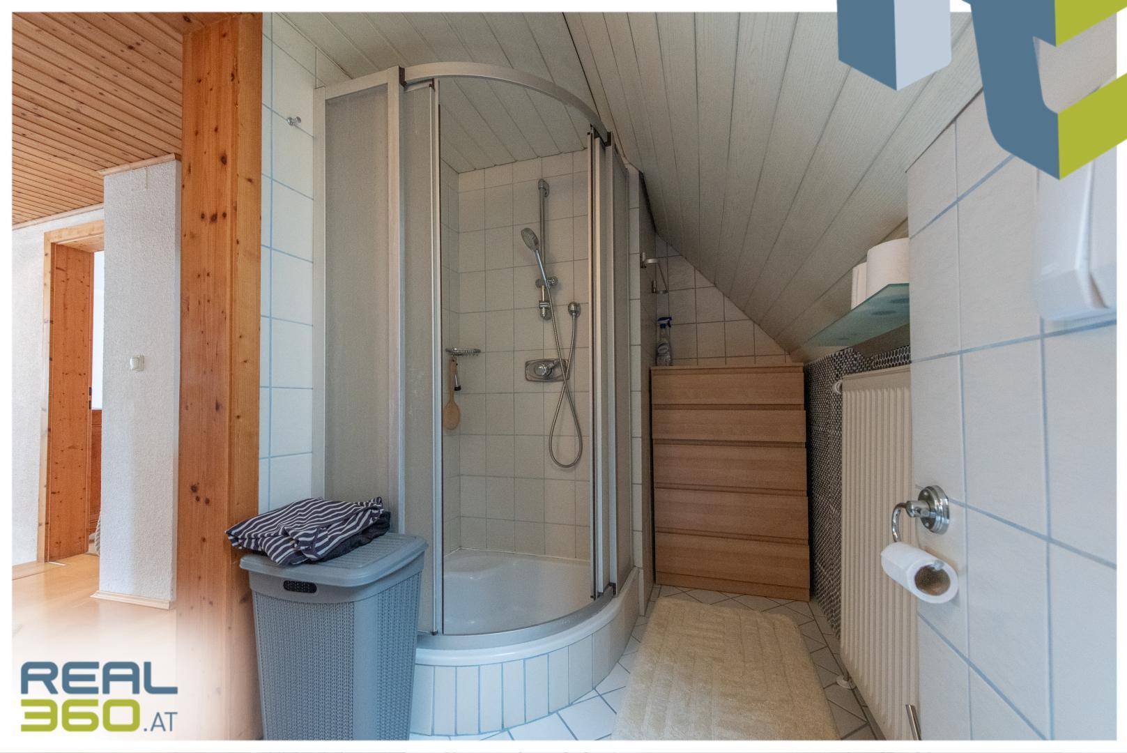Badezimmer mit Duschkabine, weißen Fliesen und Dachschräge, in gutem Zustand.