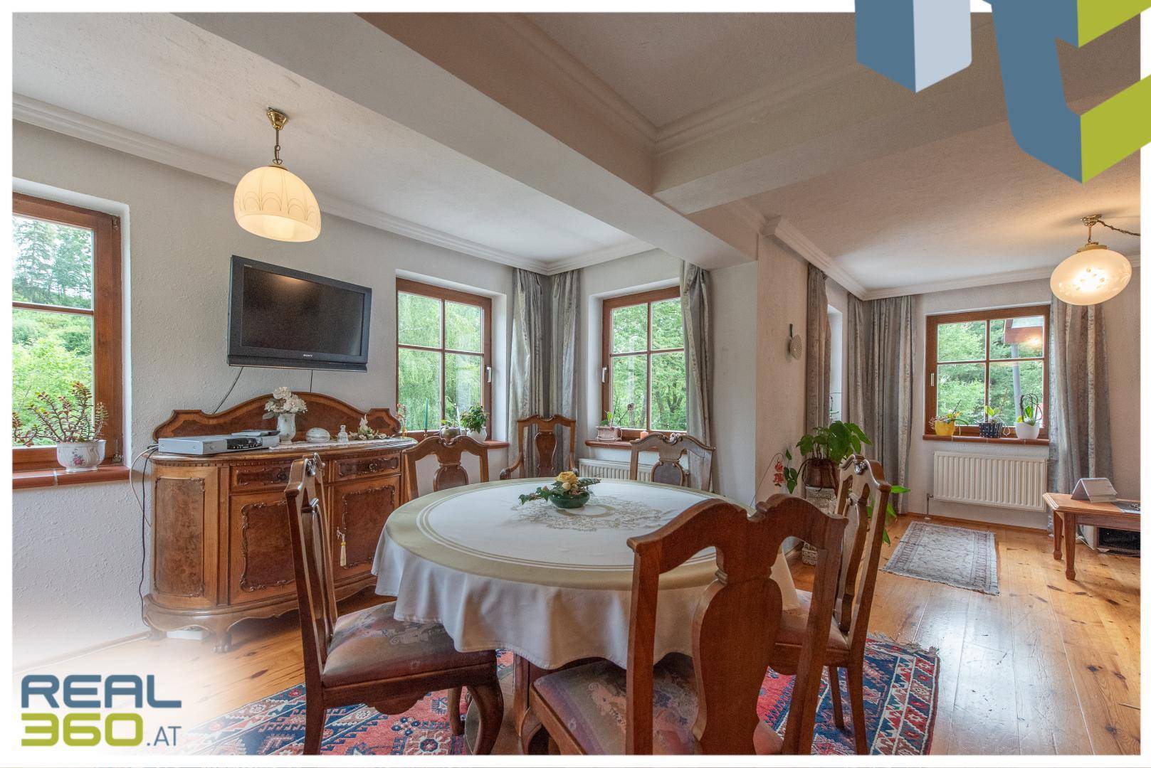 Geräumiges Esszimmer mit großem Esstisch, Holzmöbeln und Fenstern, die viel Licht hereinlassen.