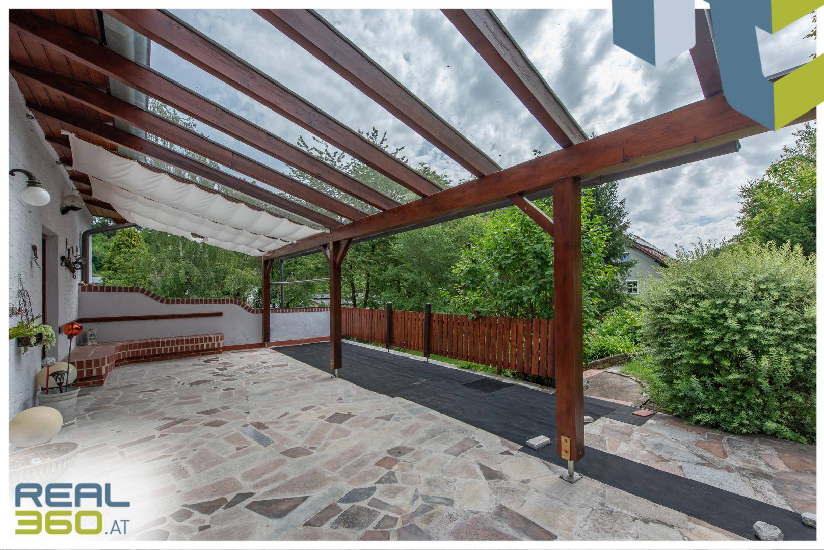 Geräumige überdachte Terrasse mit Holzpergola und Blick ins Grüne.