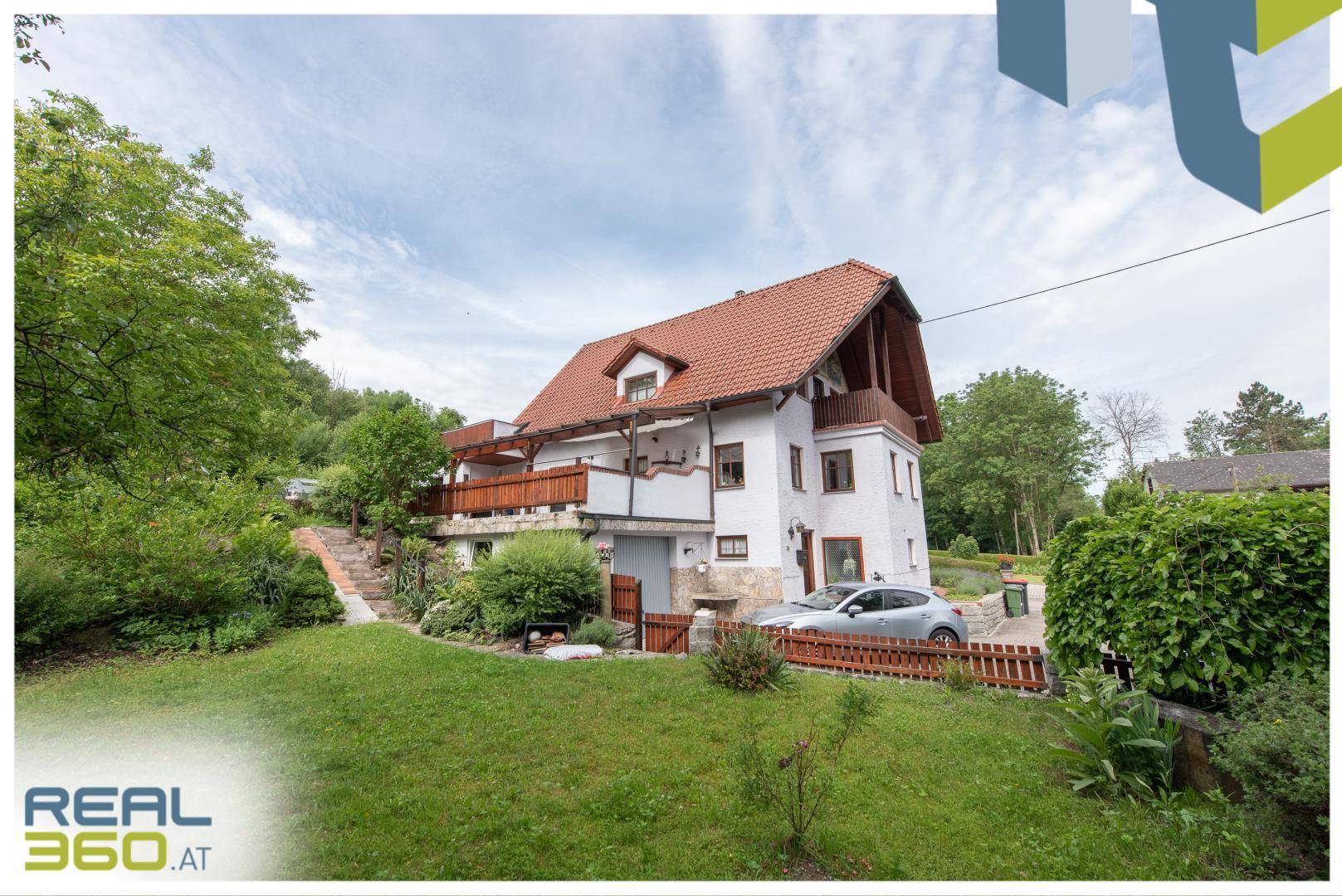Hausansicht vom Garten aus mit weißer Fassade, Holzbalkonen und einer gepflegten Rasenfläche.