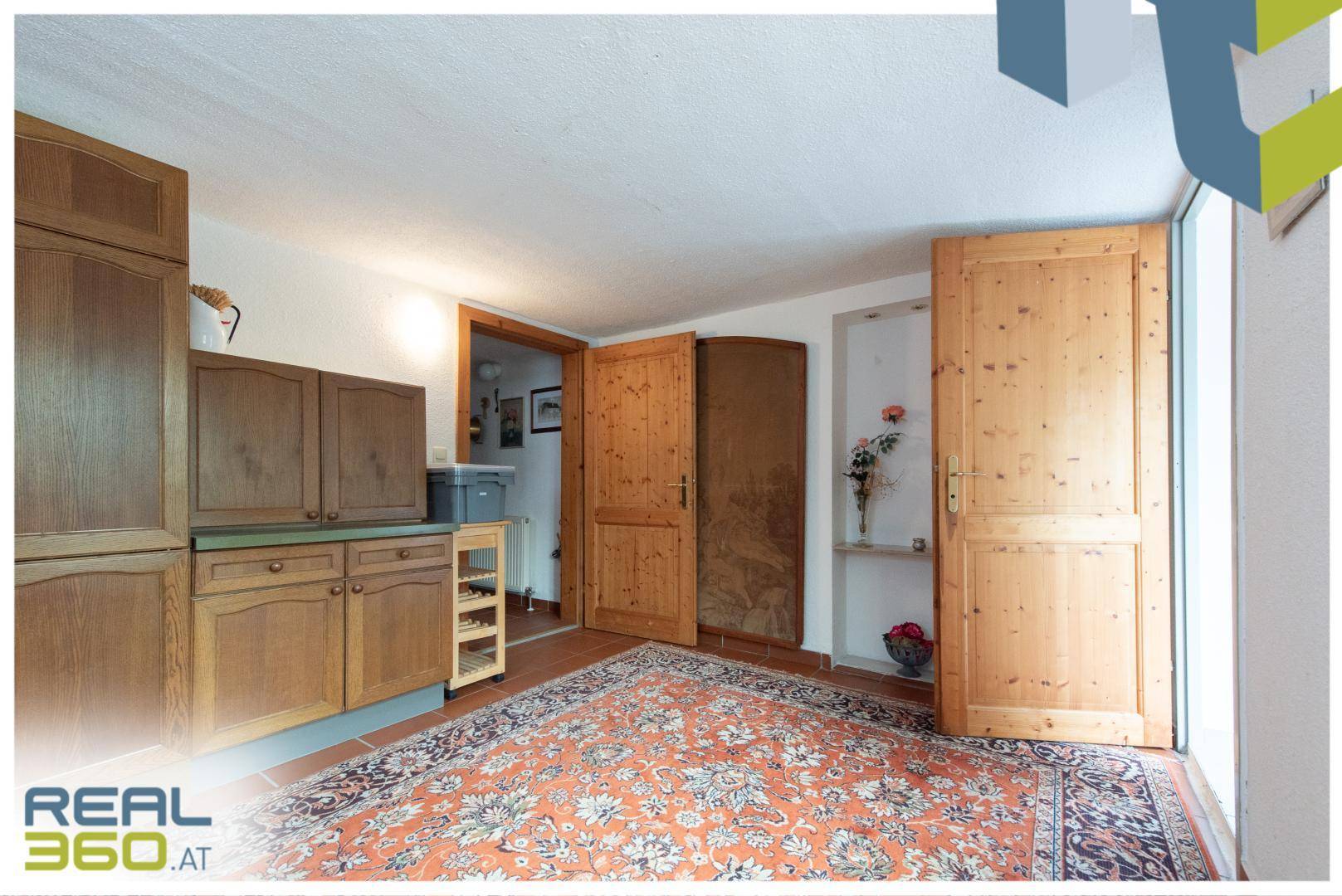 Raum mit rustikalen Holzschränken, einem gemusterten Teppich und Terrakottafliesen.