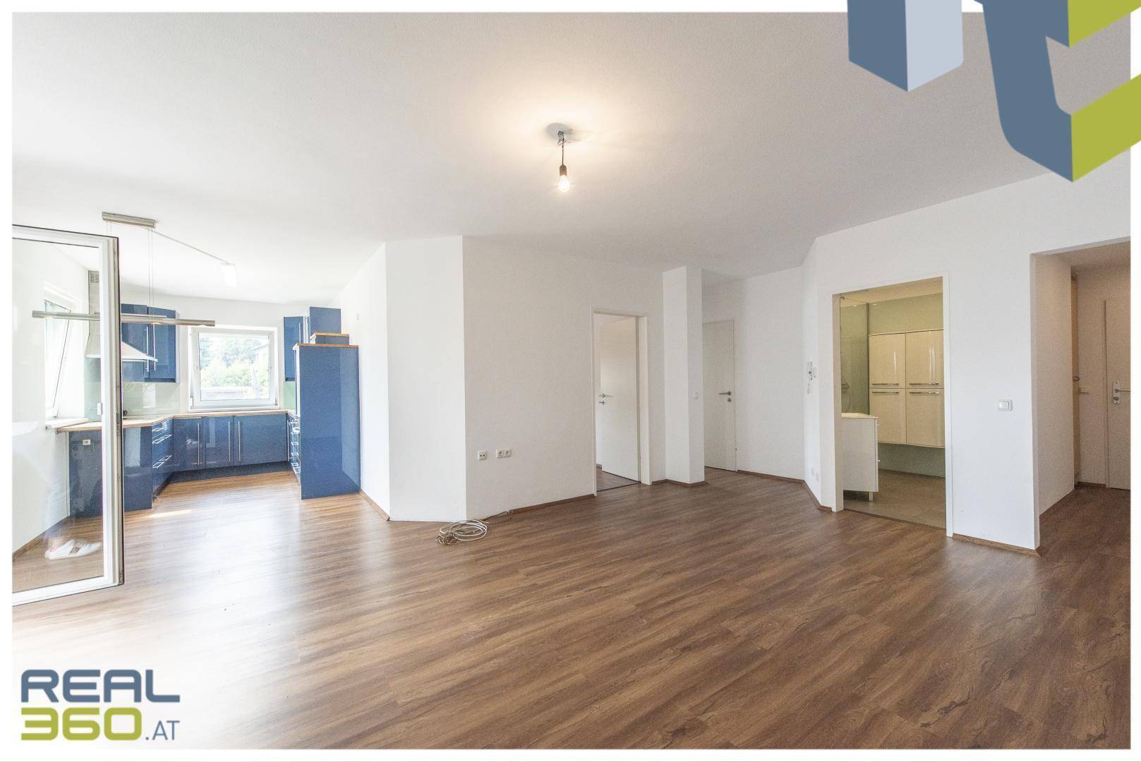 Offener Wohnbereich mit Laminatboden, Blick in die Küche und Zugang zum Badezimmer.