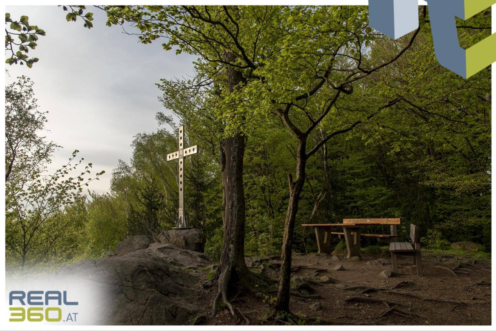 Ein Holzkreuz auf einem Felsvorsprung in einem Wald mit einem Picknicktisch und einer Bank.