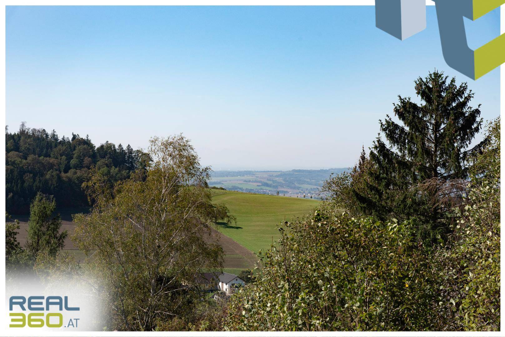 Malerischer Ausblick auf sanfte grüne Hügel, Felder und eine Siedlung in der Ferne.