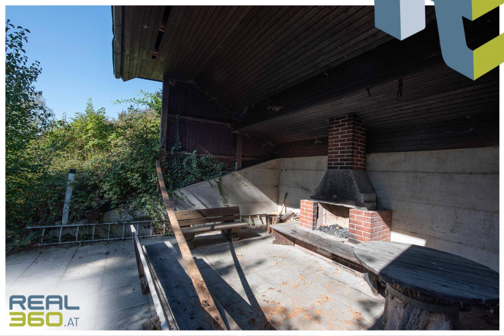 Überdachter Außenbereich mit gemauertem Kamin, Holzbänken und einem Tisch für gesellige Stunden.