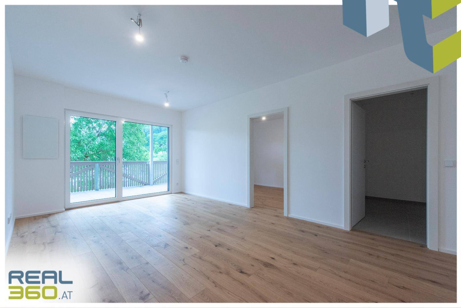 Helles Wohnzimmer mit Holzboden, großen Fenstern und Zugang zu einem Außenbereich.