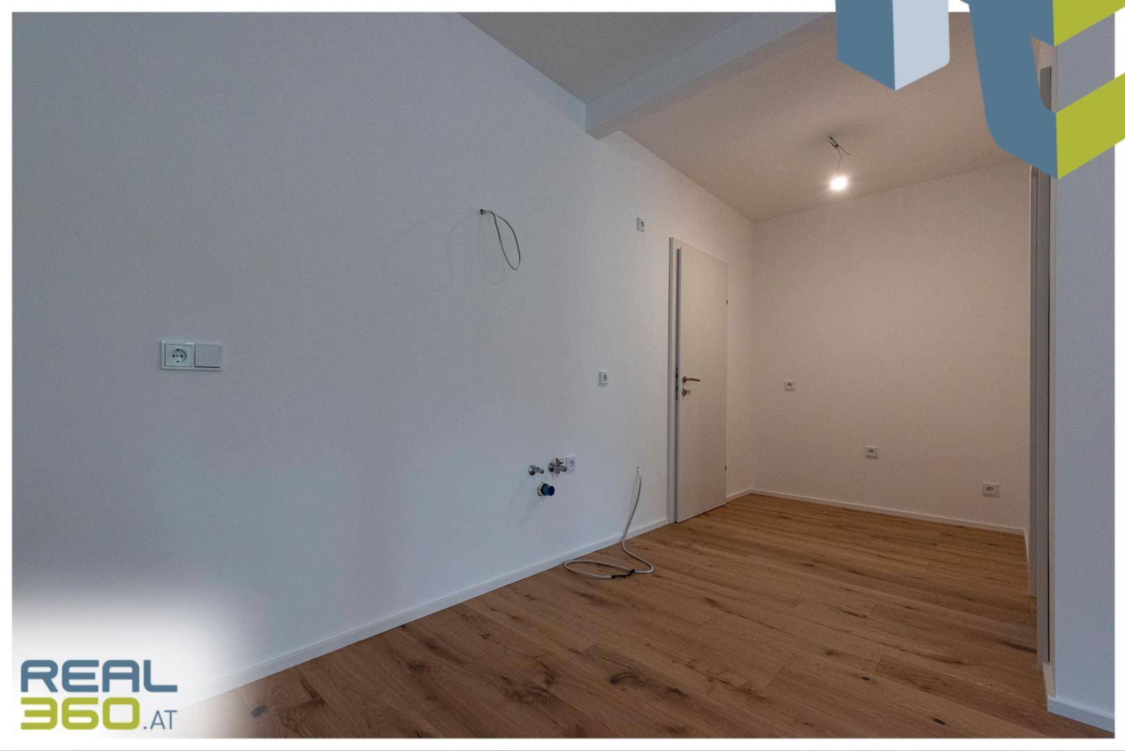 Leerer Raum mit Anschlüssen für eine Küche und hellem Holzboden.
