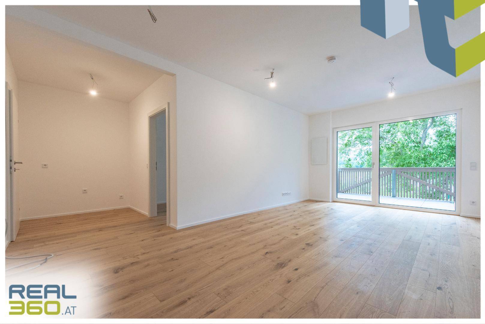 Geräumiges Wohnzimmer mit hellem Holzboden und Zugang zu einem Balkon.