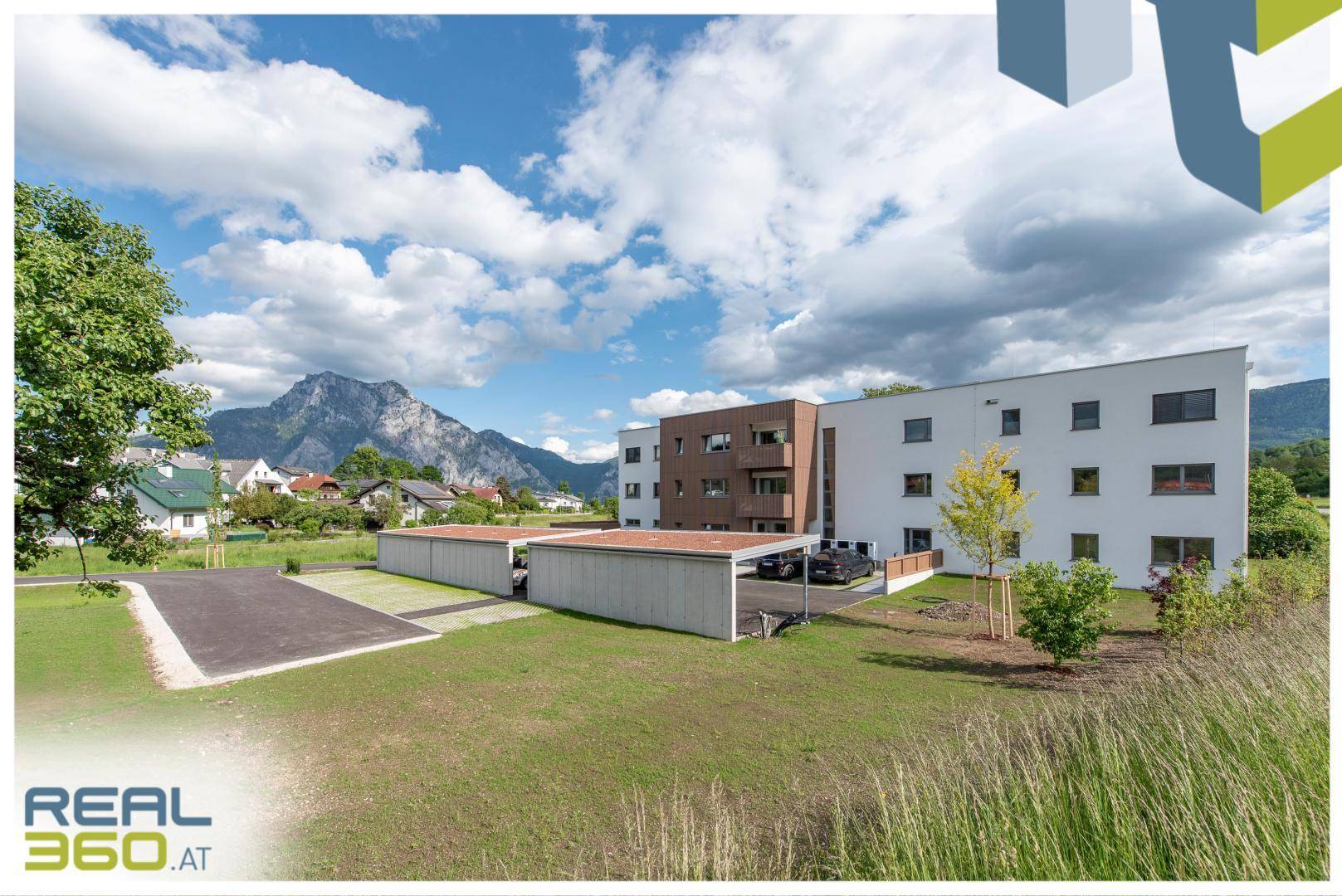 Neubau mit Parkplätzen und Carports vor einer malerischen Bergkulisse.