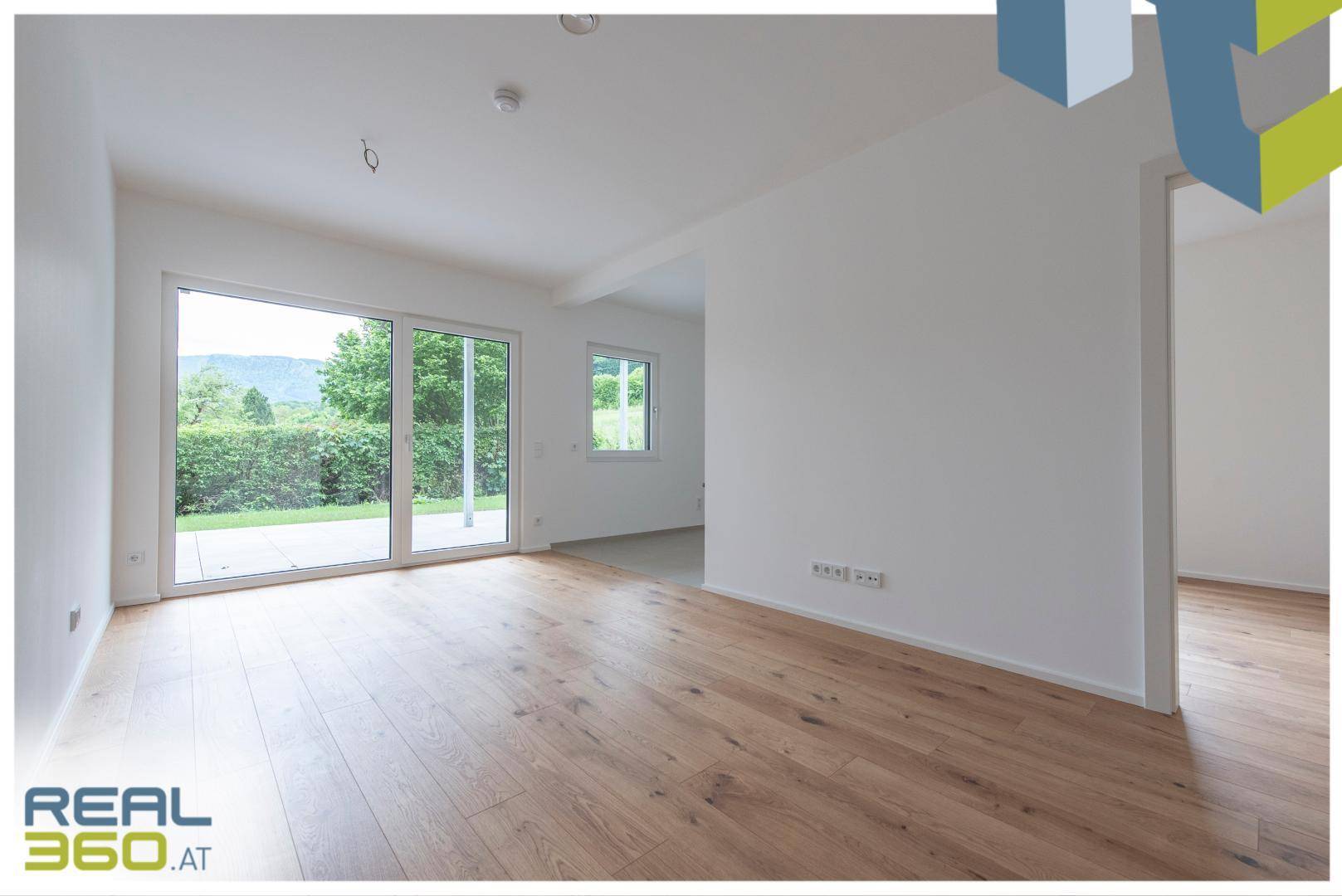 Geräumiger, heller Raum mit Holzboden und großen Fenstern mit Zugang zur Terrasse.