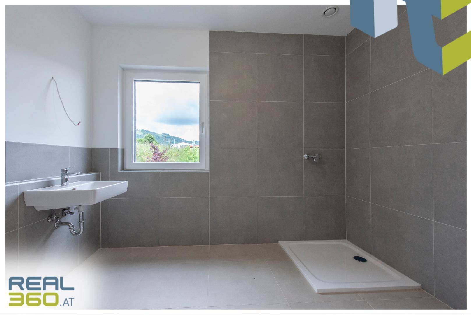 Modernes Badezimmer mit grauen Fliesen, Waschbecken und vorbereiteter Duschfläche.