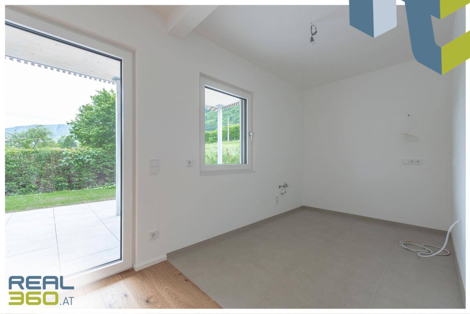 Heller Küchenbereich mit Fliesenboden und Zugang zur Terrasse, bereit für die Installation einer Küche.