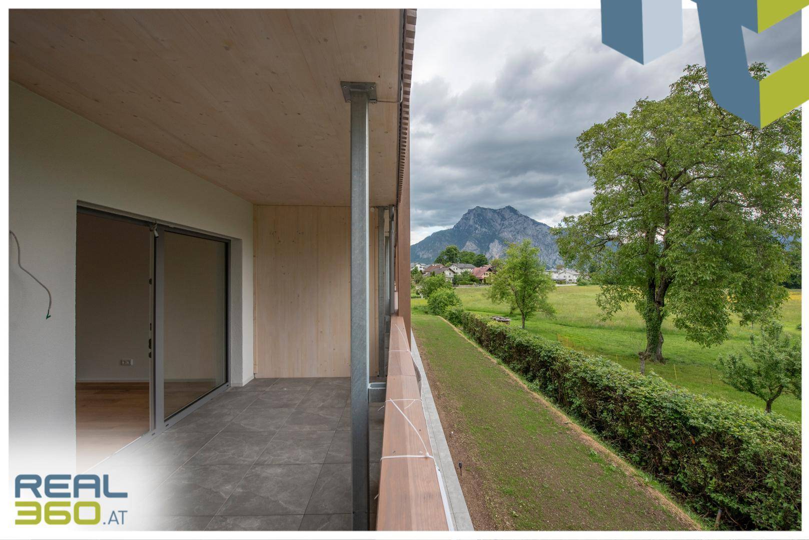 Geräumiger Balkon mit Fliesenboden und Holzelementen, bietet einen weiten Blick auf die Berge.