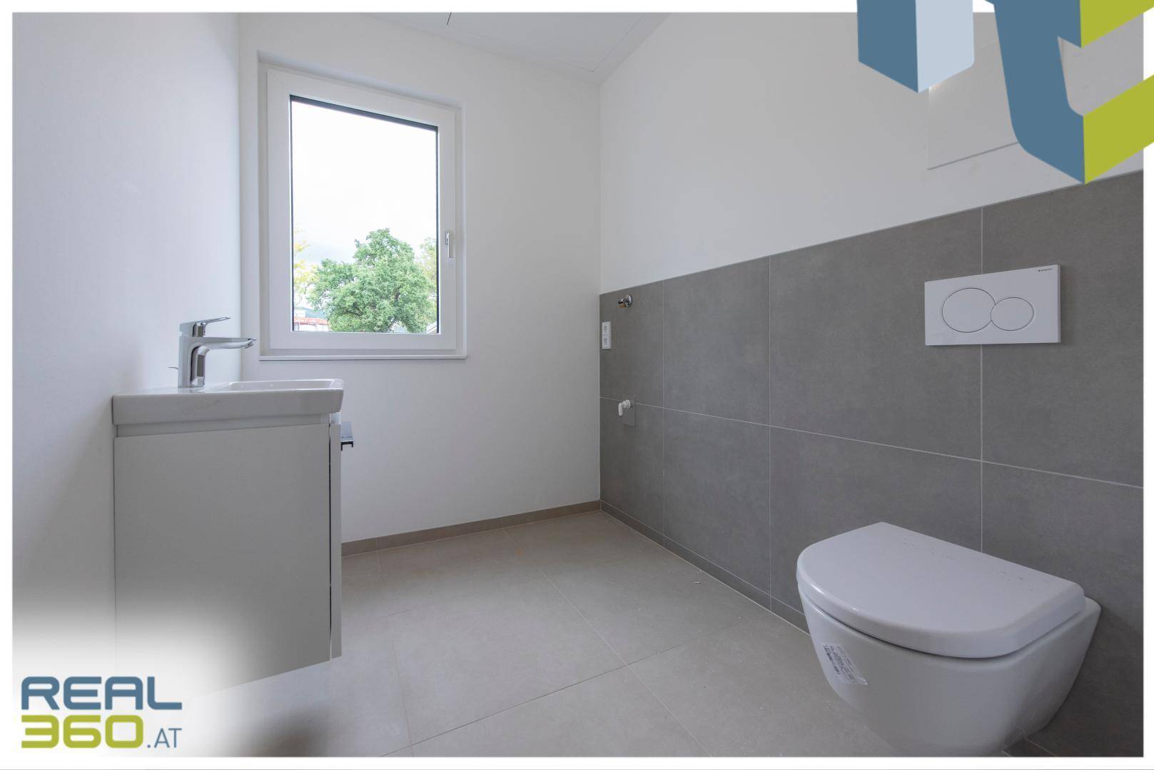 Modernes WC mit grauen Fliesen, wandhängender Toilette und kleinem Waschbecken.