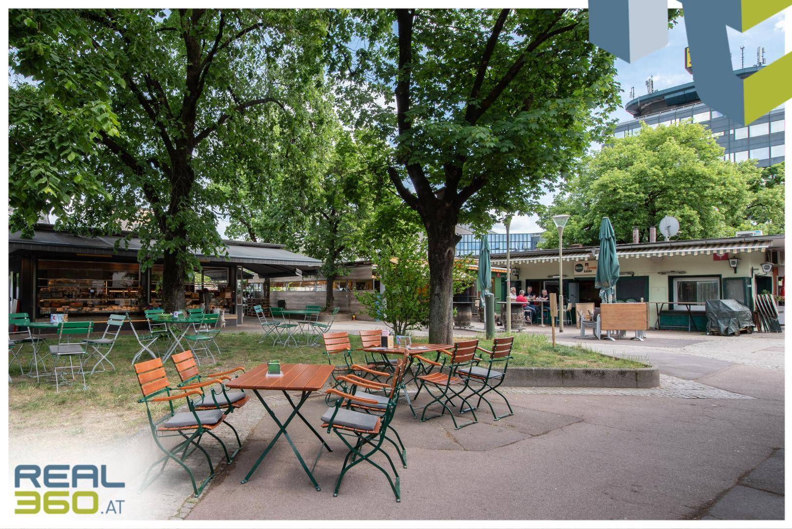 Gemütlicher Außenbereich eines Restaurants mit Holztischen und Stühlen unter Bäumen.