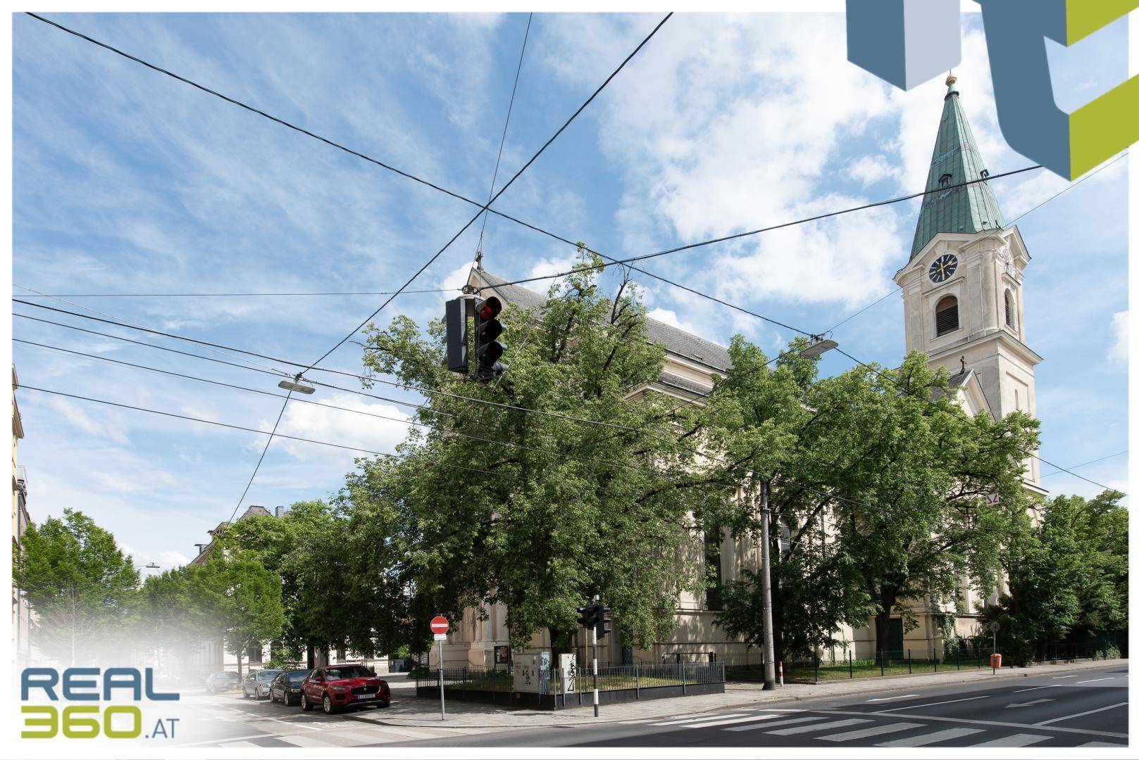 Historische Kirche mit grünem Kirchturm und umliegender Stadtlandschaft unter blauem Himmel.