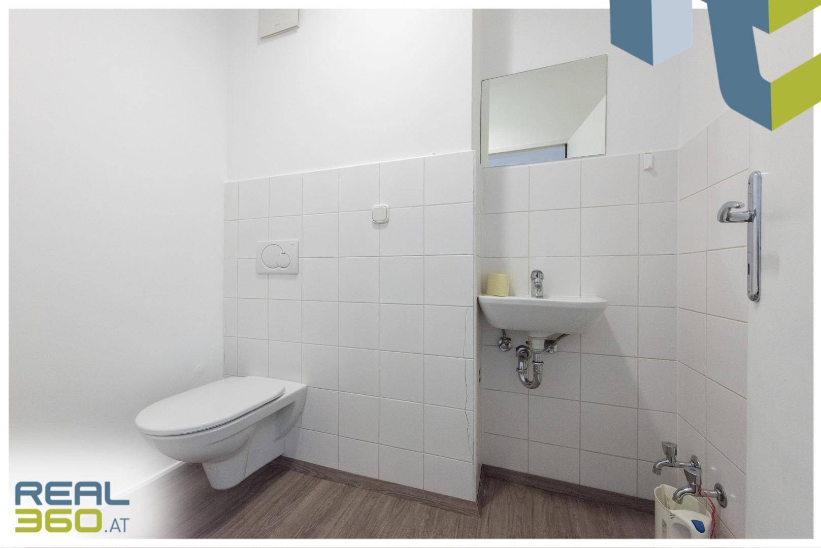 Saubere und helle Toilette mit Wand-WC, kleinem Waschbecken und weißen Fliesen.