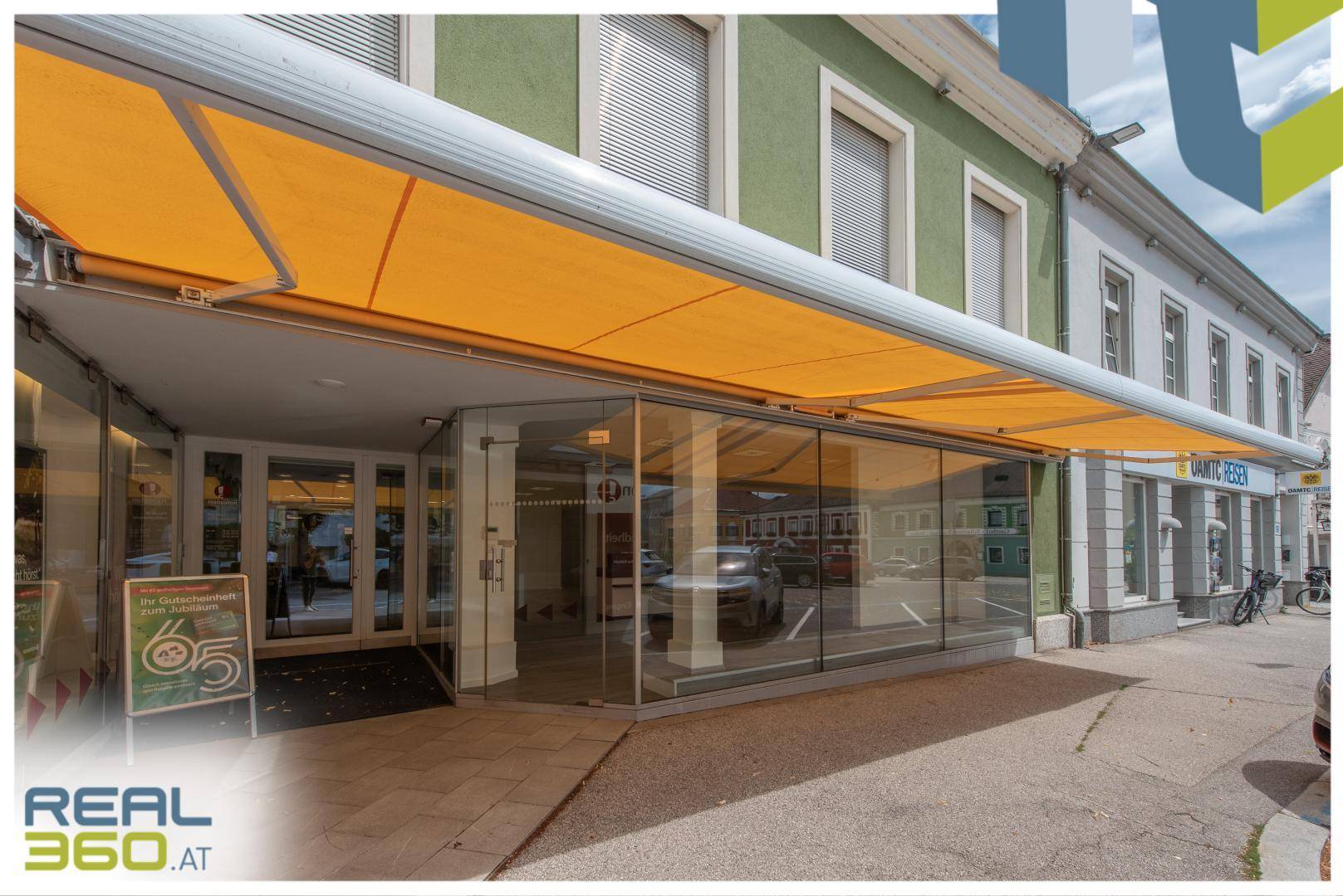 Geschäftsfassade mit ausgefahrener gelber Markise und großen Schaufenstern zur Straße.