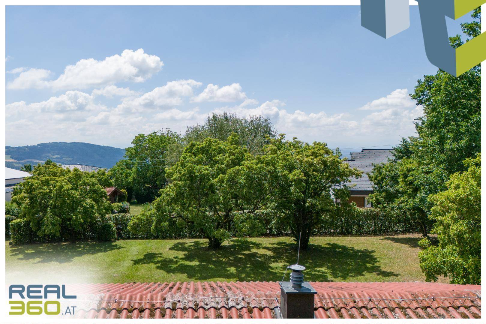 Weitläufiger Blick über den grünen Garten und das rote Dach auf die umliegende Hügellandschaft.