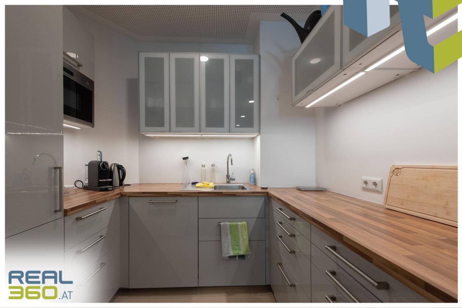 Moderne Küchenzeile mit Holz-Arbeitsplatten, grauen Schränken und integrierten Geräten.