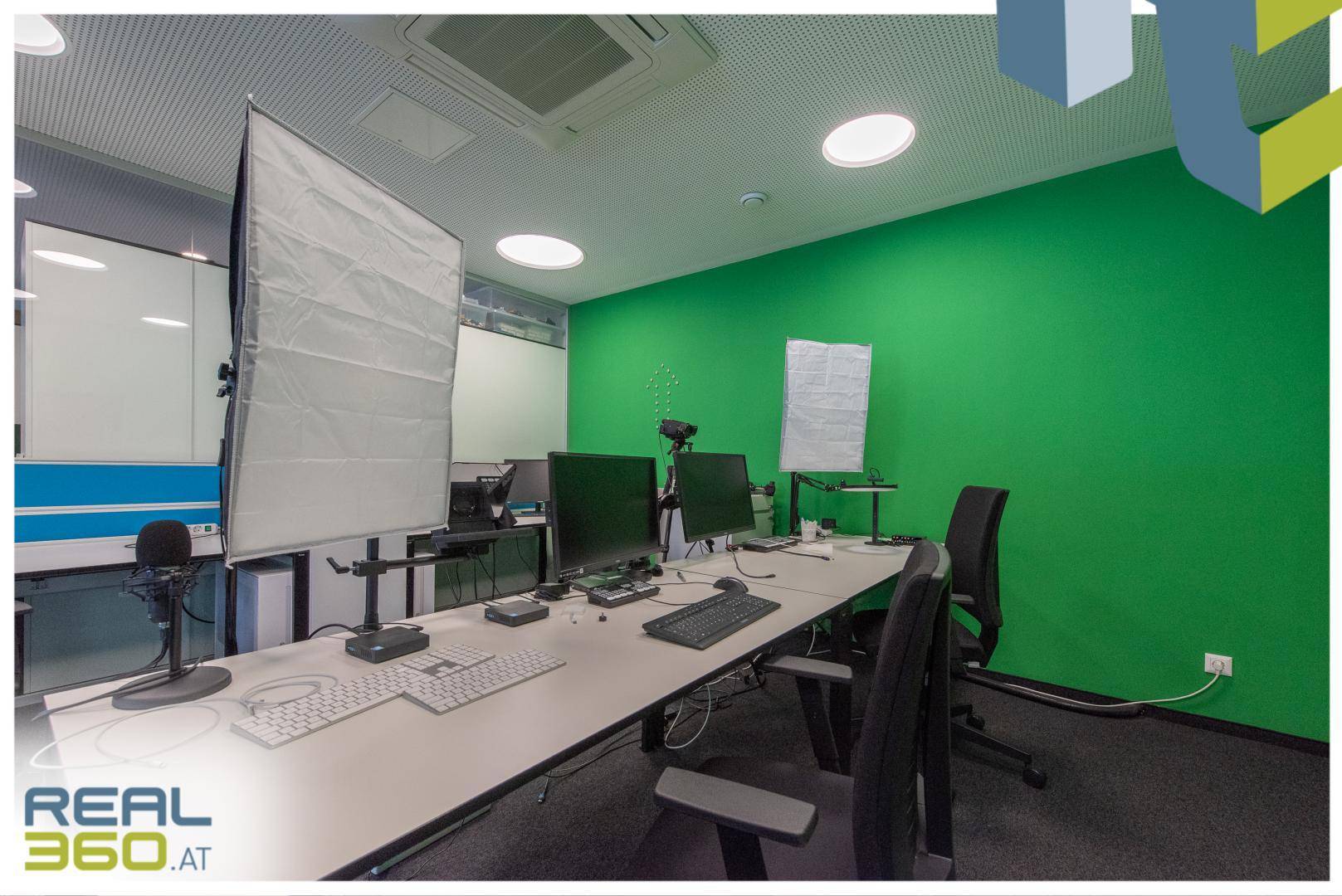Bürobereich mit grüner Akzentwand, mehreren Monitoren und professioneller Studioausrüstung.