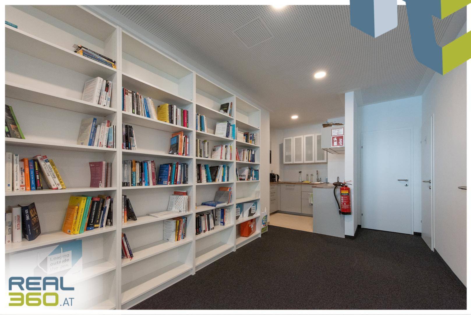 Lange Bücherregalwand führt zu einer kleinen, funktionalen Küchenzeile im Bürobereich.