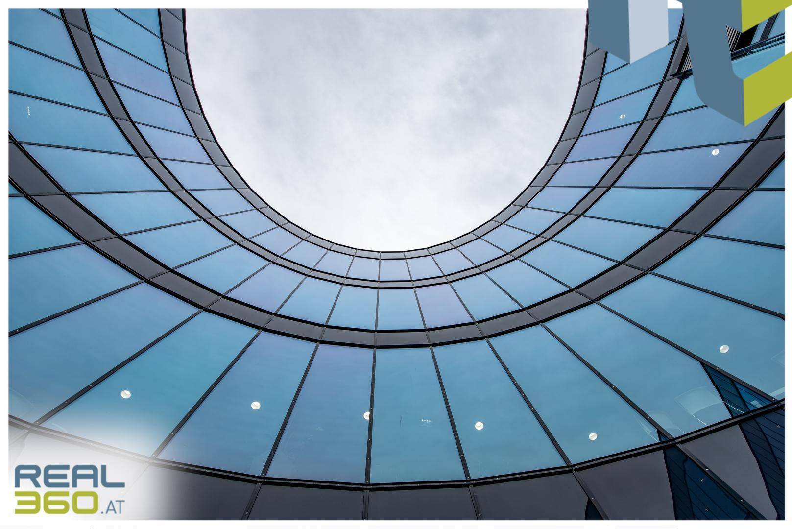 Geschwungene Glasfassade eines modernen Bürogebäudes, von unten in den Himmel ragend.