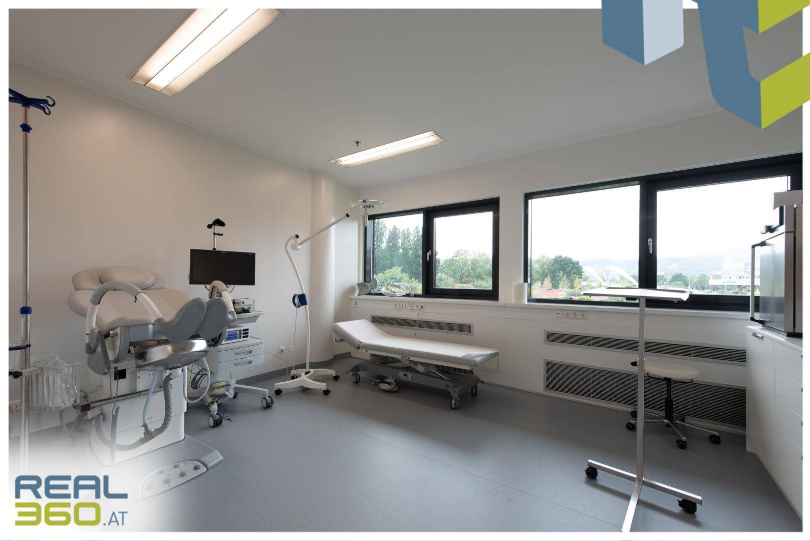 Geräumiges Untersuchungszimmer mit medizinischer Ausstattung, Liege und großen Fenstern für viel Tageslicht.