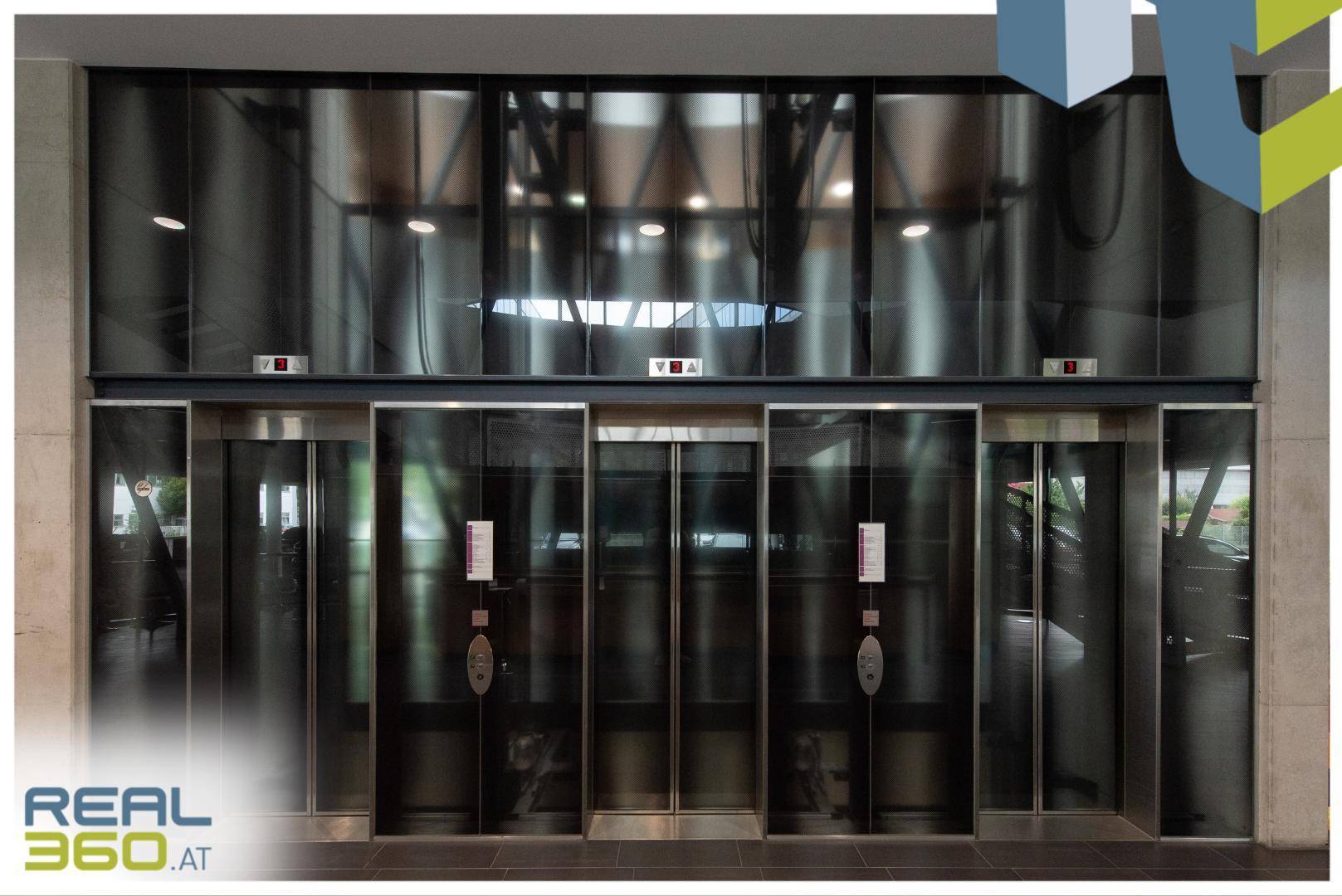 Reihe von modernen Aufzügen mit dunklen Glasfronten in einem eleganten Empfangsbereich.