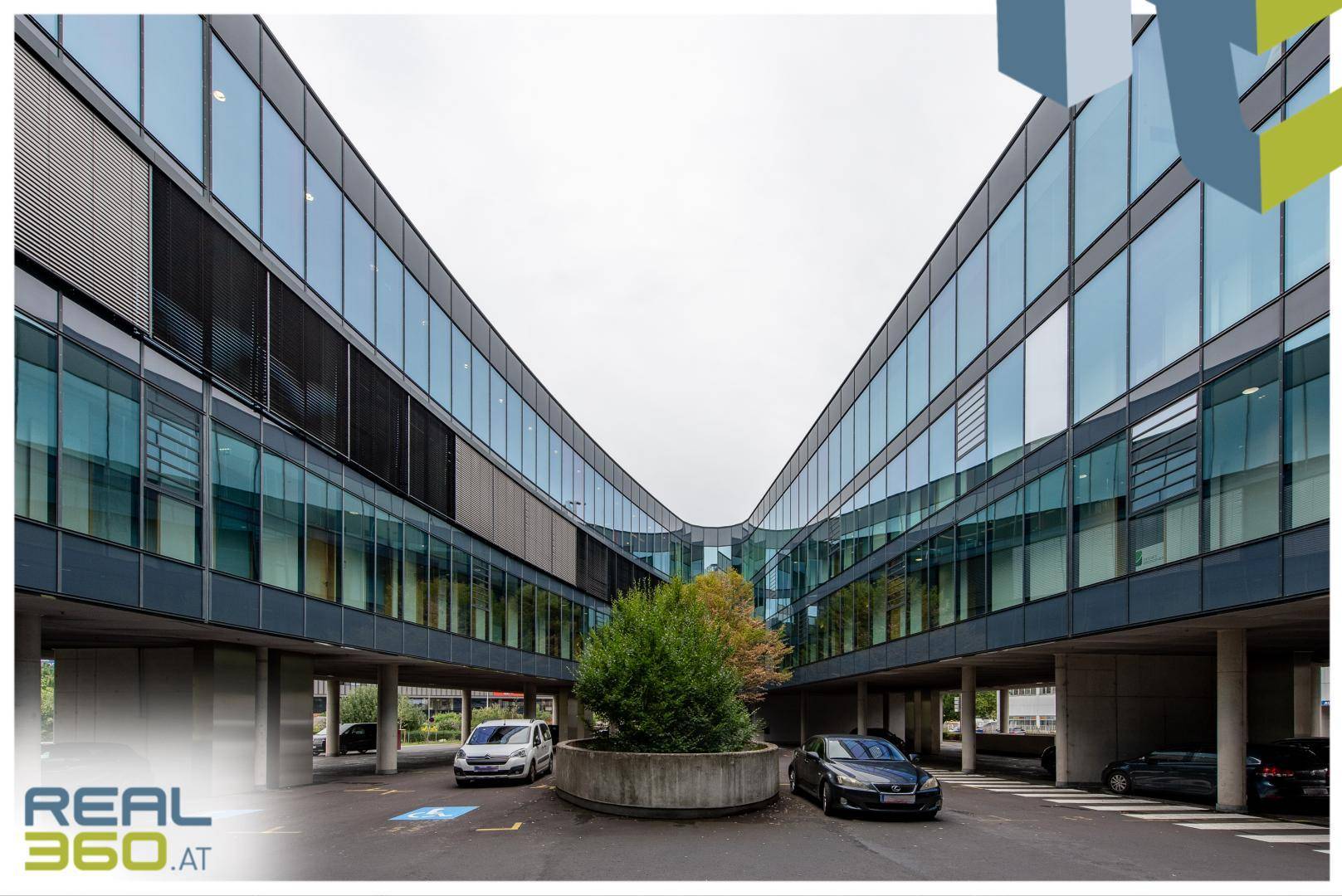 Modernes Bürogebäude mit geschwungener Glasfassade und Parkplätzen im Freien.