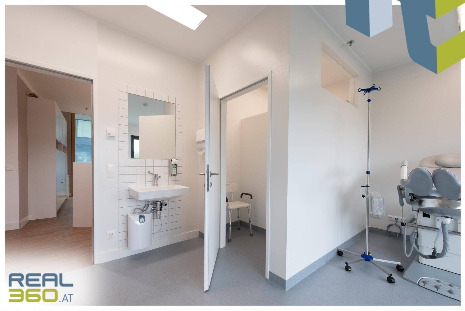 Untersuchungszimmer mit Waschbecken, Spiegel und medizinischer Liege, gut beleuchtet und funktional.