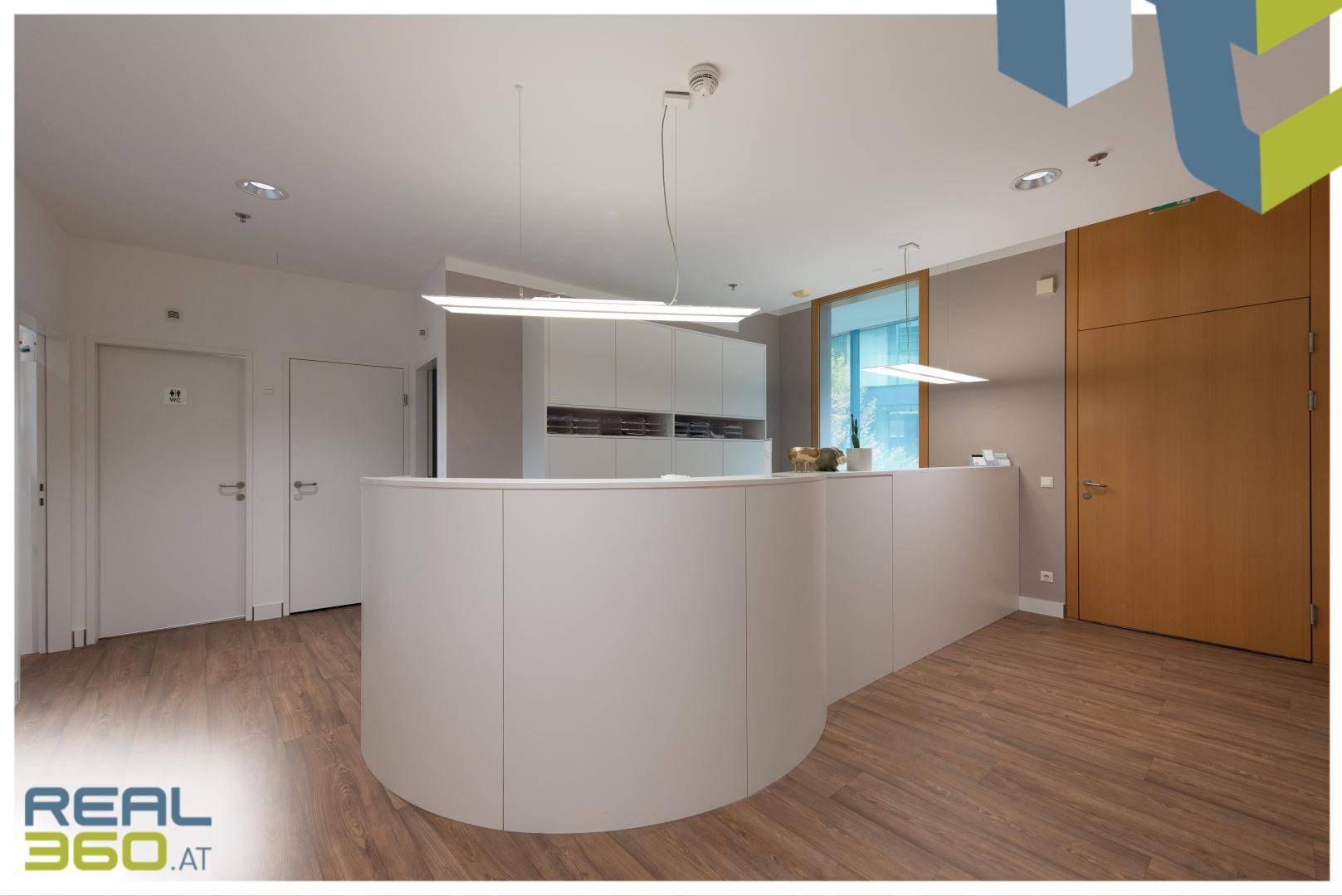 Eleganter Empfangsbereich mit geschwungener Theke, Holzboden und integrierten Schränken für Stauraum.