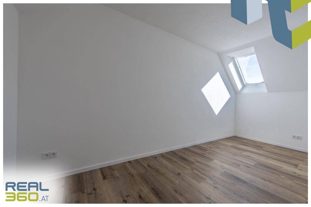 Schlafzimmer mit Dachschräge, Laminatboden und einem Dachfenster.