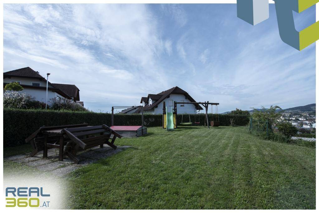 Großer Garten mit Rasenfläche, Spielplatz und Holztischgarnitur.