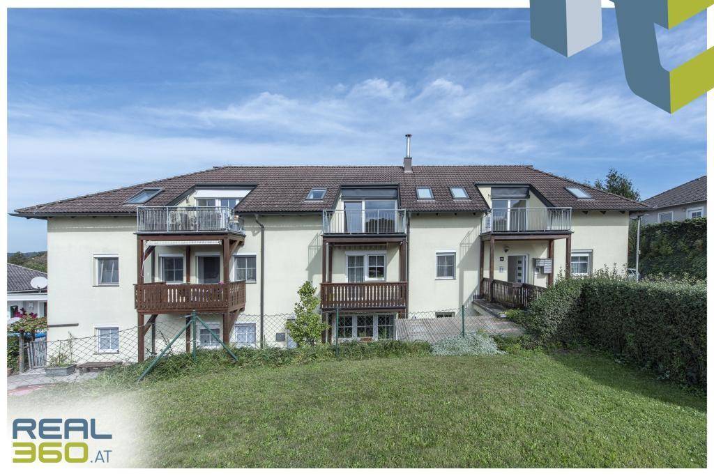 Mehrfamilienhaus mit mehreren Balkonen und Dachfenstern in ländlicher Umgebung.
